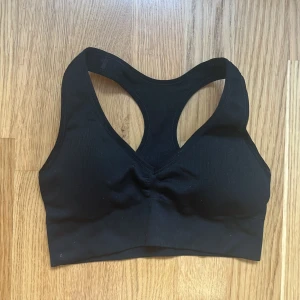 Svart sportig linnetopp XS - Svart sportig linnetopp från Stadium i storlek XS. Modellen har brottarrygg och är tillverkad i ett stretchigt syntetmaterial som passar perfekt för träning. Enkel och stilren design med liten logga bak i nacken.