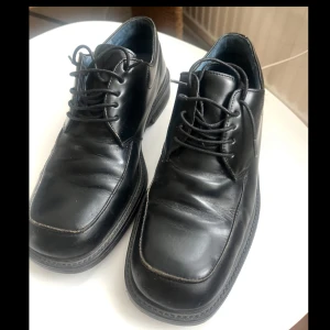 Klassiska festskor i skinn - Klassiska svarta skinnskor från Björn Borg med fyrkantig tå och snörning. Skorna har en platt sula och stilren design, perfekta för dig som gillar en clean och tidlös look. Insidan är fodrad i blått tyg för en snygg kontrast. Jättefina fest skor😊