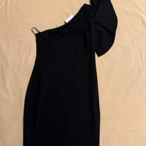 Svart oneshoulder klänning Calvin Klein - Snygg svart klänning från Calvin Klein med oneshoulder-design och puffärm på ena sidan. Stilren och elegant siluett som ger en cool vibe. Perfekt för dig som gillar minimalistisk stil med en twist. Materialet känns mjukt och följsamt mot kroppen. Nypris 1550kr