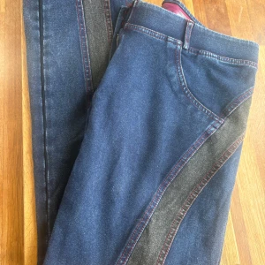 Freddy jeans med röda detaljer, storlek L - Mörkblå jeans från Freddy i samarbete med Michiko Koshino. Byxorna har röda knappar, röda sömmar och gråa paneler längs sidorna. Klassisk femficksmodell med snygg kontrast mellan blått och grått. Perfekta för dig som vill sticka ut lite extra.  Obs!! En knapp lossnat men det är bara att sy dit igen. (Se bild) 