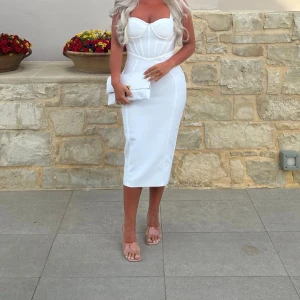 Vit figurnära långklänning med corsage - Supersnygg vit långklänning med corsage-liv och markerade sömmar som ger en riktigt smickrande siluett. Klänningen är axelbandslös och har en elegant, kroppsnära passform som framhäver formerna. Perfekt för dig som vill sticka ut med en clean och chic look.