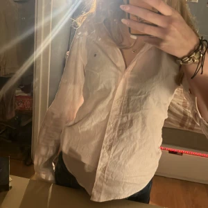 Vit och rosa randig skjorta från GANT - Säljer en stilren vit och rosa randig skjorta från GANT. Skjortan har långa ärmar och en klassisk krage. Perfekt för en elegant och avslappnad look. Passar bra till både jeans och kostymbyxor. Pris går att diskuteras (nypris cirka 1000)