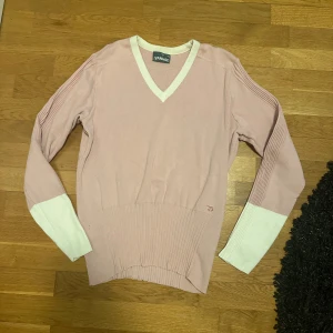 Rosa v-ringad tröja från Ivanhoe - Säljer en stilren rosa tröja från Ivanhoe med vita detaljer. Tröjan har en v-ringad hals och långa ärmar med ribbade partier. Perfekt för en avslappnad stil.