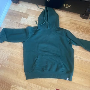 Grön hoodie med ficka - Säljer en skön grön hoodie med en stor ficka framtill. Perfekt för kyliga dagar med sin mysiga huva och långa ärmar. Passar bra för en avslappnad stil.