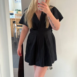 Svart klänning från Zara - Snygg svart klänning från Zara med v-ringning och korta ärmar. Perfekt för en stilren look. Klänningen har en elastisk midja för en bekväm passform.