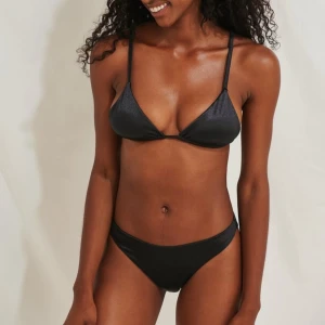Svart bikini från NA-KD - Snygg svart bikini från NA-KD med triangelformade kupor och smala axelband. Bikinin har en stilren design med en glansig finish och justerbara band för perfekt passform. Perfekt för en dag på stranden eller vid poolen.