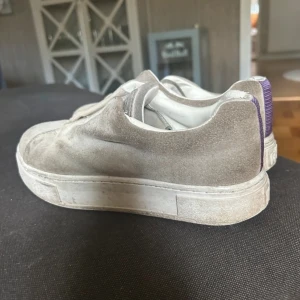 Eytys - Snygga eytys grå sneakers i mocka med en lila rand på hälen. De är köpta för 2000 kr och har använts en del. De har missfärgningar på ena sidan av skon men kan säkert gå att få bort har ej testat. Skriv för fler bilder!