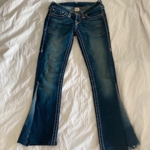 blå True Religion jeans - Snygga blå jeans från True Religion med vita kontrastsömmar och bootcut-stil. De har en knapp och dragkedja framtill samt klassiska fem fickor. Perfekta för en avslappnad look. 💞Midjemått är 33 cm. 🙏🏻