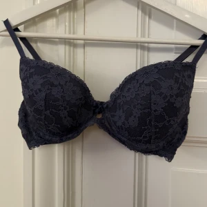 Mörkblå/grå spets-bh från H&M - Elegant bh från H&M med vacker spetsdetaljering. Den har justerbara axelband och en bekväm passform. Perfekt för att ge en lyxig känsla till vardagsoutfiten.