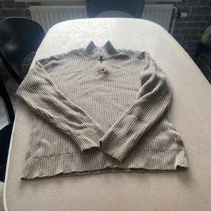 Grå ribbad tröja från Calvin Klein Jeans - Säljer en stilren grå ribbad tröja från Calvin Klein Jeans. Tröjan har en dragkedja framtill och en hög krage som ger en modern look. Perfekt för kyligare dagar. Passar bra till både jeans och chinos.