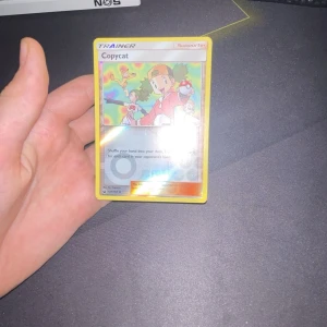 Pokémonkort - Copycat Trainer - Säljer ett Pokémonkort av typen Trainer med namnet Copycat. Kortet har en färgglad illustration på framsidan och den klassiska Pokémon-baksidan med en Pokéball. Perfekt för samlare eller spelare som vill förstärka sin kortlek.