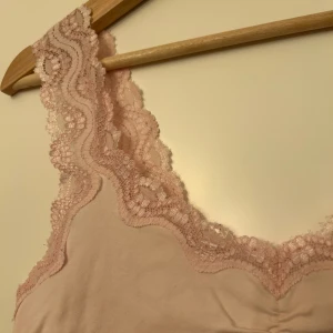 Rosa linne med spetsdetaljer, y2k-känsla - Mjukt, sött rosa linne med vackra spetsdetaljer längs axelbanden och halsringningen. Perfekt att stylea snyggt. Nästan perfekt skick! Köpt second hand så lappen finns ej kvar och jag har aldrig testat linnet, men gissar på storlek S.