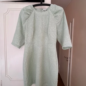 Pistagegrön klänning från Twist & Tango - Säljer en elegant ljusgrön klänning från Twist & Tango med ett subtilt mönster. Klänningen har trekvartsärmar och en dragkedja i ryggen. Perfekt för en stilren look! Knappt använd