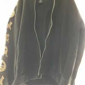 Svart hoodie med tryck - Svart fullzip hoodie med dragkedja ända upp och detaljer på ärmarna. Köpt på new yorkers herr avdelning i somras.
