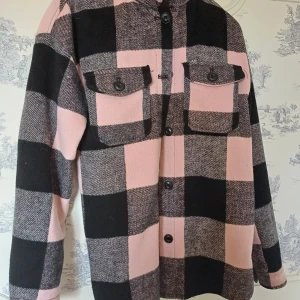 Rutig overshirt i rosa och svart - Snygg och trendig overshirt i rosa och svart med stora rutor. Jackan har knappar framtill och två bröstfickor med lock. Perfekt för lager-på-lager-stilen.