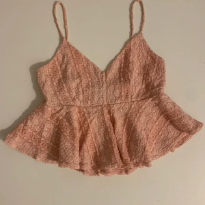 Rosa spetslinne - Säljer ett sött rosa spetslinne med smala axelband och volangdetaljer från TopShop. Perfekt för sommarens varma dagar. Linnet har en v-ringad design och är tillverkat i ett lätt och luftigt material.
