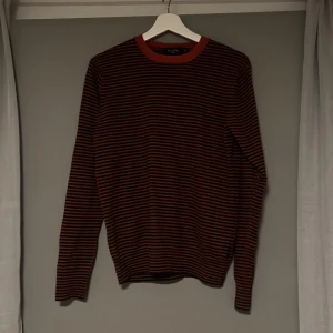 Randig tröja - Säljer en snygg randig tröja från Paul Smith i svart och röd. Tröjan har långa ärmar och en rund halsringning. Perfekt för en stilren look.