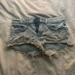lågmidjade jeansshorts  - Säljer ett par ljusa jeansshorts från H&M med fransiga kanter och slitna detaljer. Shortsen har en normal passform och är perfekta för sommardagar. De har en knapp och dragkedja framtill samt klassiska fem fickor.