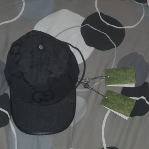 Svart keps från Gucci - Snygg svart keps från Gucci med diskret GG-mönster. Kepsen har justerbart spänne baktill för perfekt passform. Tillverkad i Italien med högkvalitativt material.