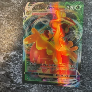 Flapple VMAX Pokémonkort - Säljer ett holografiskt Flapple VMAX Pokémonkort med 320 HP och attacken G-Max Rolling. Kortet har en färgglad design med Flapple i fokus och är en del av VMAX-serien. Perfekt för samlare eller spelare som vill förstärka sin kortlek. Äkta. Pris kan diskuteras 