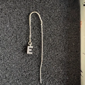 Silverörhänge med hängande E - Säljer detta superfina hängande öronhänget med silvriga stenar och bokstaven E. Sparsamt använt och köptes från l8hasselblad.