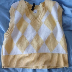 Stickade västar i gult och grönt - Två stickade västar i olika mönster och färger. Den första är gul och vit med ett rutigt mönster och v-ringning. Den andra är grön och vit med ett zebramönster och rund hals. Båda har ribbade kanter och är croppade. Säljs tillsammans 