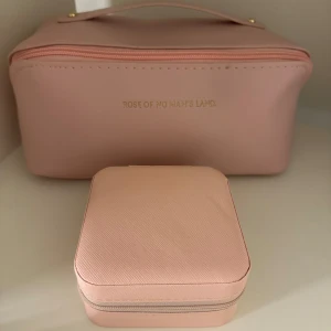 Rosa necessär och smyckeskrin - Säljer en stilren rosa necessär och matchande smyckeskrin från Rose of No Man's Land. Necessären har en dragkedja och ett praktiskt handtag. Smyckeskrinet har flera fack för smycken och en mjuk insida. Perfekt för att hålla ordning på dina accessoarer.helt nya