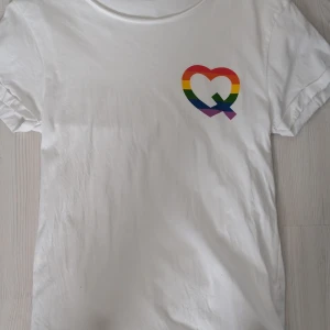 Vit t-shirt med regnbågshjärta - Säljer en oversized vit t-shirt med ett färgglatt regnbågshjärta på bröstet. T-shirten har korta ärmar och är gjord i mjukt bomullsmaterial. Perfekt för en avslappnad stil.