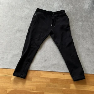 Svarta mjukisbyxor från Hoodrich - Säljer ett par svarta mjukisbyxor från Hoodrich. Byxorna har en avslappnad passform med snörning i midjan och ribbade muddar vid bensluten. Väldigt sköna. Passar ca 170-180. Hör av er vid minsta fundering😁✌️