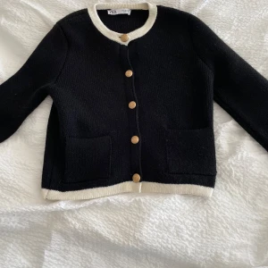 Svart kofta från Zara - Säljer en stilren svart kofta från Zara med kontrasterande vita kanter och snygga knappar i guld. Koftan har långa ärmar och m fickor framtill. Perfekt för en elegant look. Säljes då den ej kommer till användning, köpt för 300💕