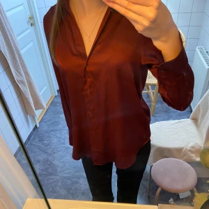 Vinröd Blus - Vinröd blus av satin med knappar framtill.
