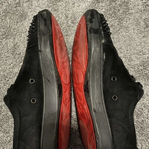 Svarta sneakers med nitar - Snygga svarta sneakers med nitar på tån och röd sula. Skorna har snörning och en stilren design som sticker ut. Det kommer ej med box eller kvitto och lite slitna där fram som man kan se på bilden!!