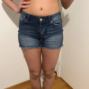 Blå jeansshorts från Only - Snygga blå jeansshorts från Only med fransiga kanter. De har en klassisk femficksdesign och knappgylf. Perfekta för en avslappnad stil. Midejemått tvärsöver 35cm