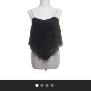 Svart chiffonglinne med spetsdetaljer - Elegant svart chiffonglinne med vita spetsdetaljer på axelbanden. Toppen har en luftig och fladdrig design som ger en fin rörelse. Perfekt för en stilren och chic look. Skulle säga att den är ganska liten i storleken.