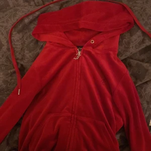 Röd hoodie från Juicy Couture - Säljer en snygg röd hoodie från Juicy Couture med dragkedja och broderad logga på bröstet. Den har en justerbar huva och är tillverkad i ett mjukt material som ger en bekväm känsla. 