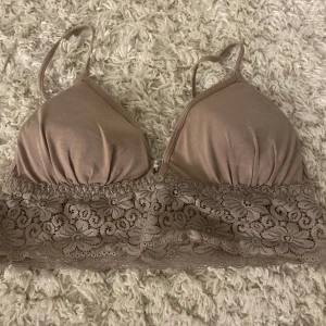 Beige spetsprydd bralette - Säljer en snygg beige bralette med spetsdetaljer. Den har smala axelband och en vacker spetskant nedtill som ger en romantisk touch. Perfekt för att bära under en lös topp eller som den är för en avslappnad look.