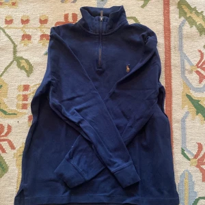 Marinblå half zip från Polo Ralph Lauren - Snygg marinblå långärmad tröja från Polo Ralph Lauren med half zip och klassisk broderad logga på bröstet. Tröjan är i bomull och har en hög krage som ger en clean och sportig look. Perfekt för lager-på-lager och chill vardagsstil.