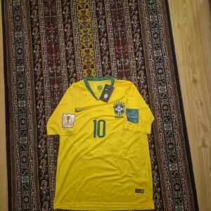 Brasilien Neymar Jr VM 2018 tröja Nike - Säljer en officiell Brasilien fotbollströja från VM 2018 med Neymar Jr och nummer 10 på ryggen. Tröjan är gul med gröna detaljer, har korta ärmar och FIFA World Cup patch på armen. Tillverkad i lätt och ventilerande Dri-Fit material. Perfekt för fans av landslaget!