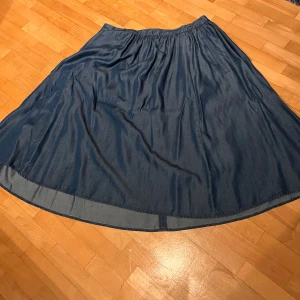 Blå kjol från Boss Orange - Blå vadlång kjol från Boss Orange med mjukt, lätt material och ett enkelt, flowy fall. Inte mycket använd. Kjolen har en klassisk midja och två praktiska fickor. Spetsdetalj på insidan av midjan. 