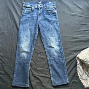 Replay blå jeans straight fit - Snygga blå jeans från Replay med klassisk straight fit och fem fickor. Jeansen har en mörkblå tvätt med lätt slitningar framtill och bak, samt Replay-lapp i skinn baktill i midjan. Perfekta för dig som gillar en tidlös och clean look.