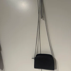 Grå axelväska med kedjerem - Grå axelväska med stilren design och silverfärgad kedjerem. 