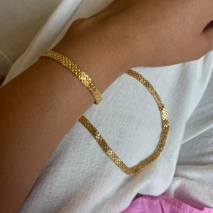 Guldigt halsband och armband set - Snyggt set X-länk med halsband och armband i guldton. Båda har platt, glittrande kedja som fångar ljuset och ger en lyxig känsla. Perfekt för att lyfta vilken outfit som helst. Lås i metall för enkel användning. Passar dig som gillar stilrena accessoarer med lite extra bling. Vattentålig, rekomenderas att inte ha kontakt med vatten längre tid, går bra tvätta händer och vid vardagliga aktiviteter. Vill du att det ska hålla sin lyster i årtal, kontakta ej me kemikalier, som parfym med mera. 