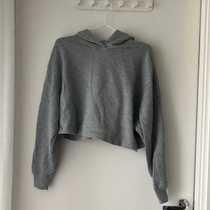 Grå croppad hoodie från ASOS 4505 - Snygg grå croppad hoodie från ASOS 4505 med huva och långa ärmar. Tröjan har en loose passform och är gjord i mjuk bomullsmix, perfekt för en chill och avslappnad stil. Enkel och stilren design som funkar till många outfits.