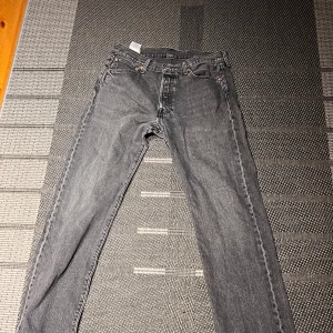 Levi's 501 svarta jeans W34 L32 - Klassiska svarta Levi's 501 jeans med rak passform och knappgylf. Klippt där nere så det ska se snyggare ut på skor. Jeansen har fem fickor och är tillverkade i robust denim. Snyggt tvättad svart färg som ger en cool vintage vibe. Perfekta för dig som gillar tidlös stil.