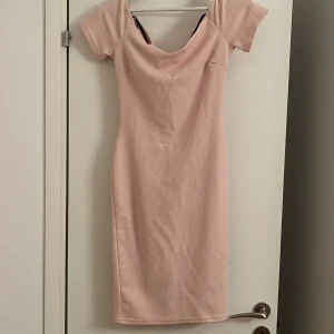 Ljusrosa ribbad kortklänning med twist - Säljer en ljusrosa kortklänning med ribbad struktur och slim passform. Klänningen har korta ärmar och en snygg twistad detalj med öppen rygg baktill. Perfekt för dig som gillar en feminin och trendig look. Materialet känns mjukt och stretchigt.