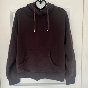 Mörkbrun hoodie med huva och ficka - En oversized mörkbrun hoodie med stor ficka framtill och huva med snörning. Tröjan har långa ärmar och ribbade muddar vid ärmslut och nederkant. Perfekt för chill dagar eller när du vill ha en enkel och stilren look.