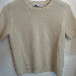 Beige stickad tröja från Zara - Säljer en stilren beige stickad tröja från Zara. Tröjan har korta ärmar och en rund halsringning. Perfekt för en avslappnad och chic look. Passar bra till både jeans och kjol.