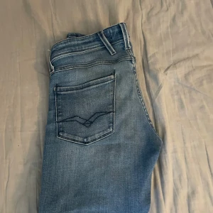 Replay Anbass ljusblå jeans - Säljer ett par Replay Anbass jeans i ljusblå tvätt med klassiska fem fickor och snygga detaljer på bakfickorna. Jeansen har normal passform och är tillverkade i mjukt denimtyg med lite stretch för extra komfort. Perfekta för en avslappnad och stilren look.