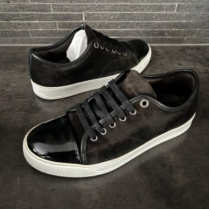 Svarta sneakers från lanvin  - Snygga svarta sneakers med ovandel i mocka och glansig lackad tå. Storlek ut 5 sitter runt 40. Skorna är i bra skick inga defekter. Hör av er vid frågor 