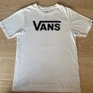 Vit Vans t-shirt  - Vit t-shirt från Vans i klassisk passform, storlek M JR . T-shirten har korta ärmar och en stor svart Vans-logga tryckt på bröstet. Motagare står för frakt
